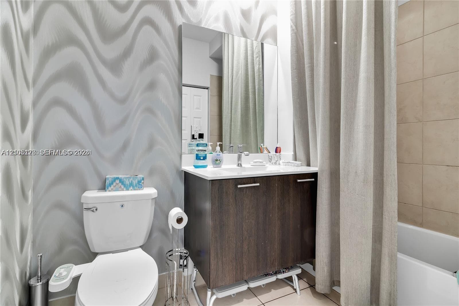 Bathroom featuring a dark wood-finish vanity with a white countertop, an integrated sink, a wall-mounted rectangular mirror, and neutral wall-tile surrounds