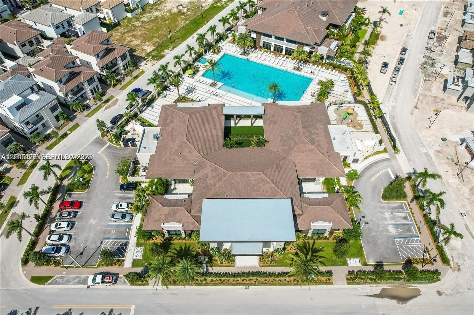 Community center featuring a multi-lane swimming pool, landscaped central courtyard, paved surface parking, and curated palm tree installations