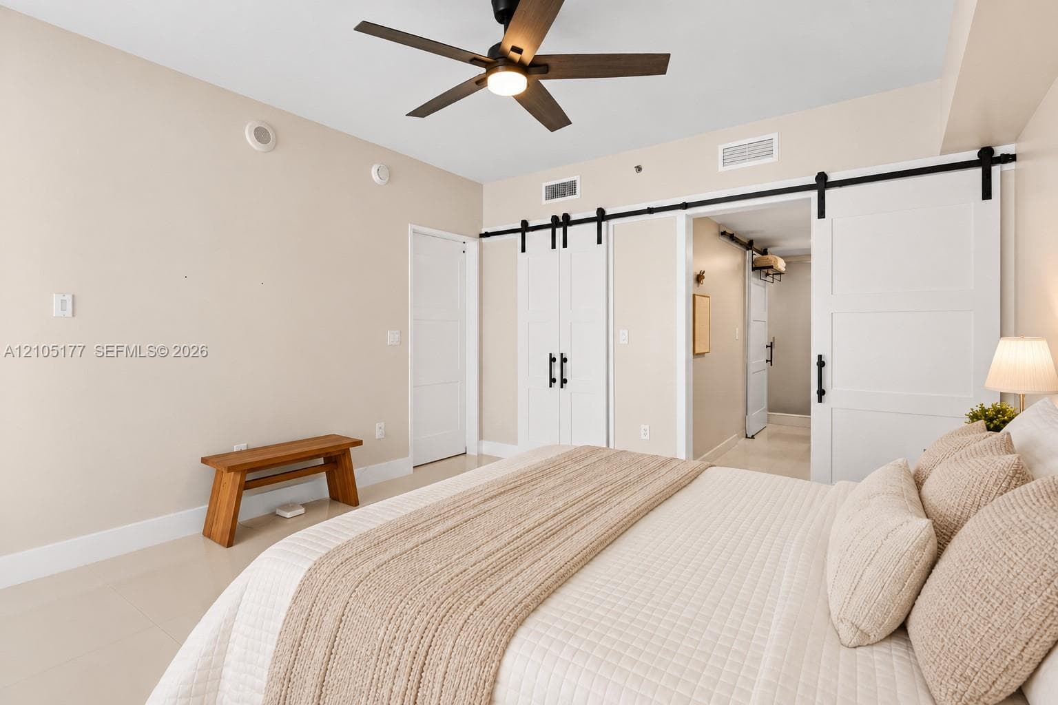 Neutral wall palette featuring white barn-style sliding doors with matte black hardware, recessed ceiling lighting, and a dark-finish ceiling fan