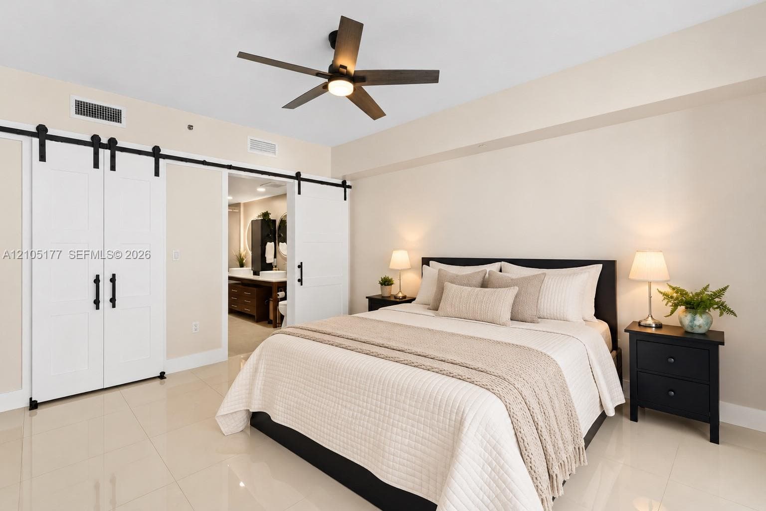 Neutral-toned room featuring large-format tile flooring, white sliding barn-style doors with matte black hardware, and a modern ceiling fan with integrated lighting