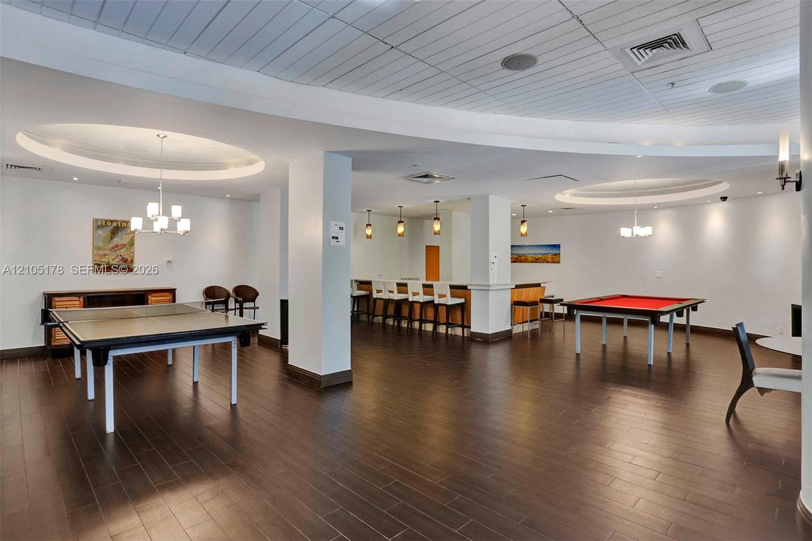 Open-concept interior featuring wood-finish flooring, recessed circular tray ceilings with decorative light fixtures, and a built-in bar with pendant lighting