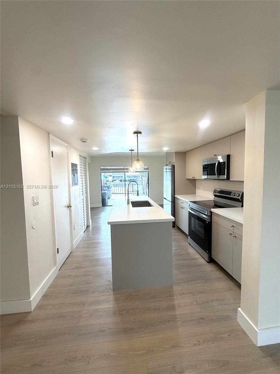 Modern kitchen featuring wood-finish flooring, white countertops, and stainless steel appliances