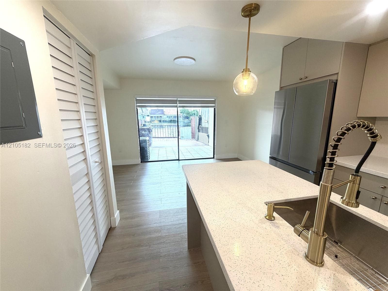 Kitchen island with integrated sink and modern gold-tone faucet, stainless steel refrigerator, contemporary pendant lighting, and sliding glass doors opening to an outdoor area