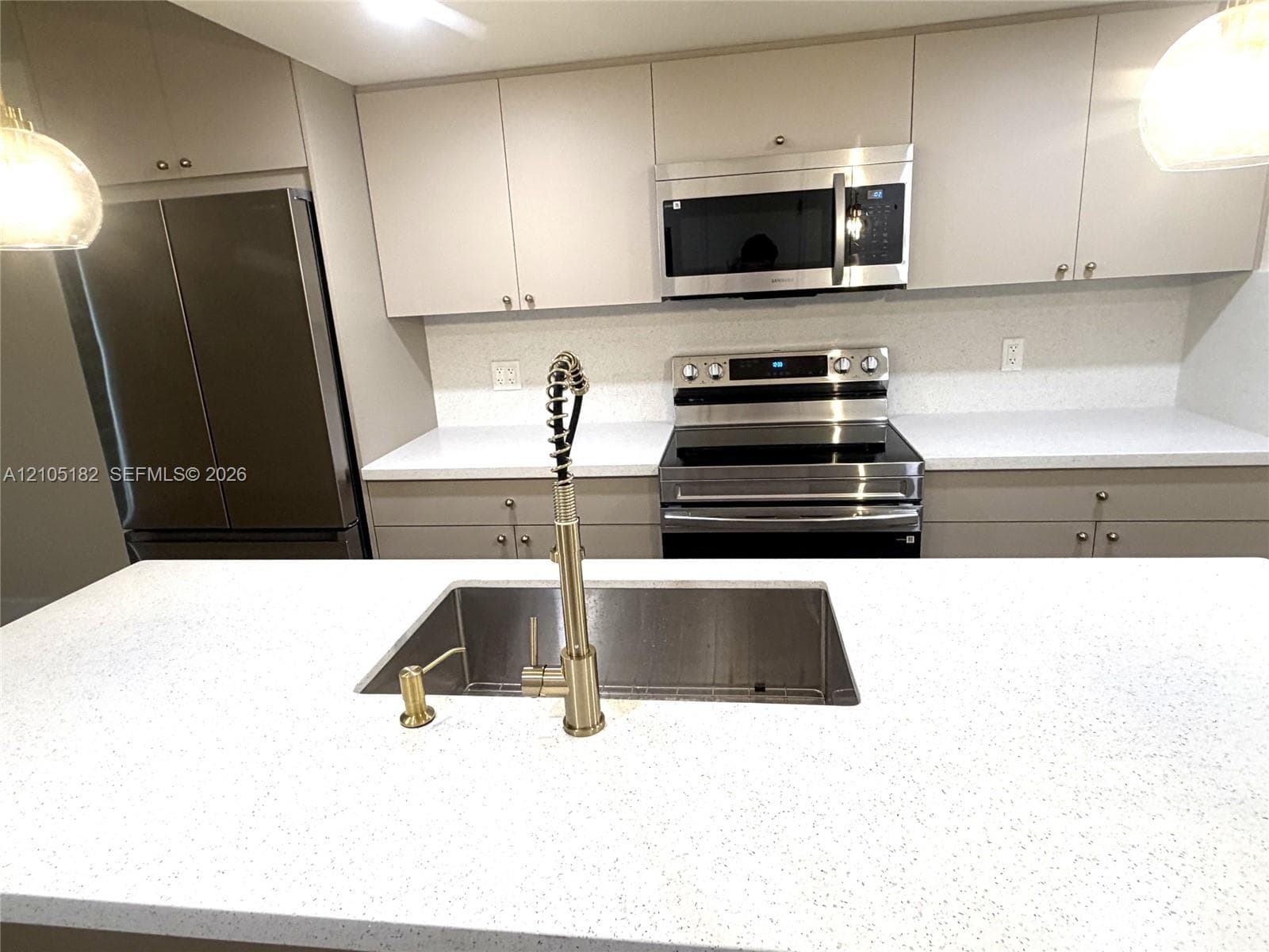 Kitchen featuring light-toned cabinetry, stainless steel appliances, white countertops, and a stainless steel sink with a gold-tone faucet