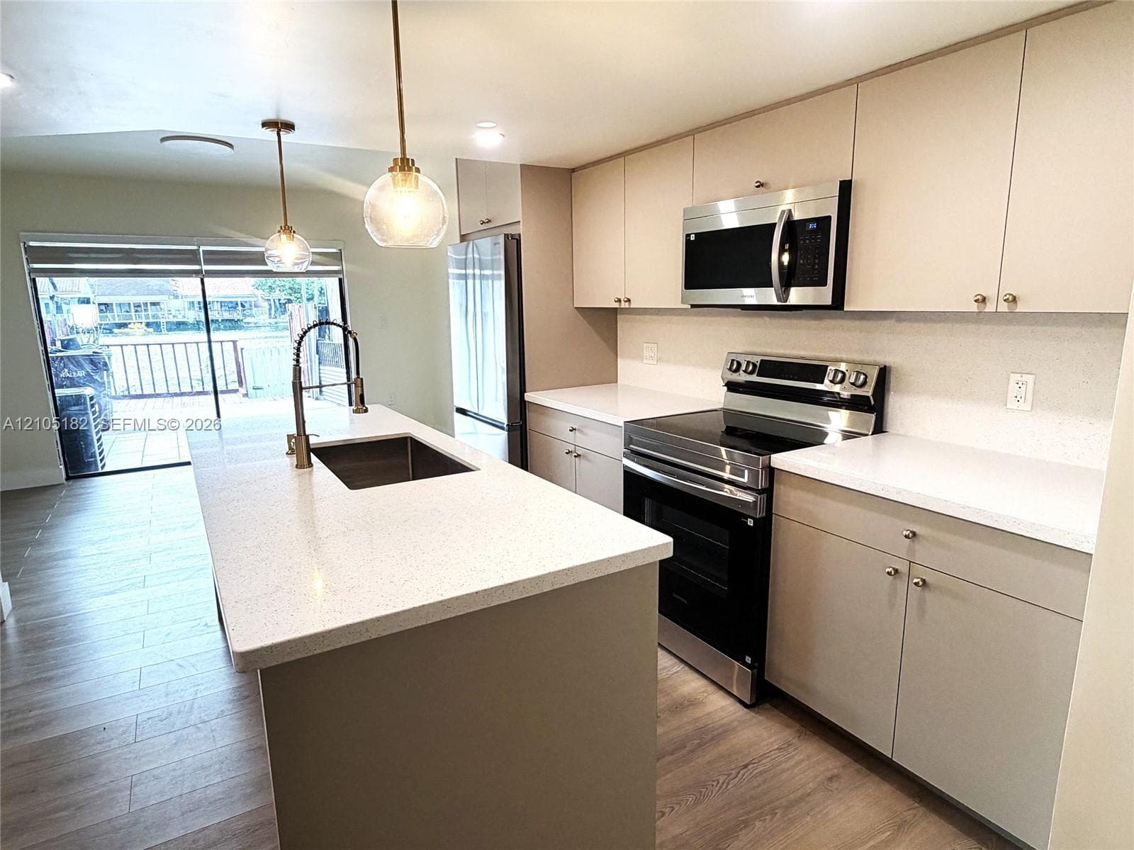 Kitchen featuring a center island with an undermount sink, pendant lighting, wood-finish flooring, white countertops, and stainless steel appliances