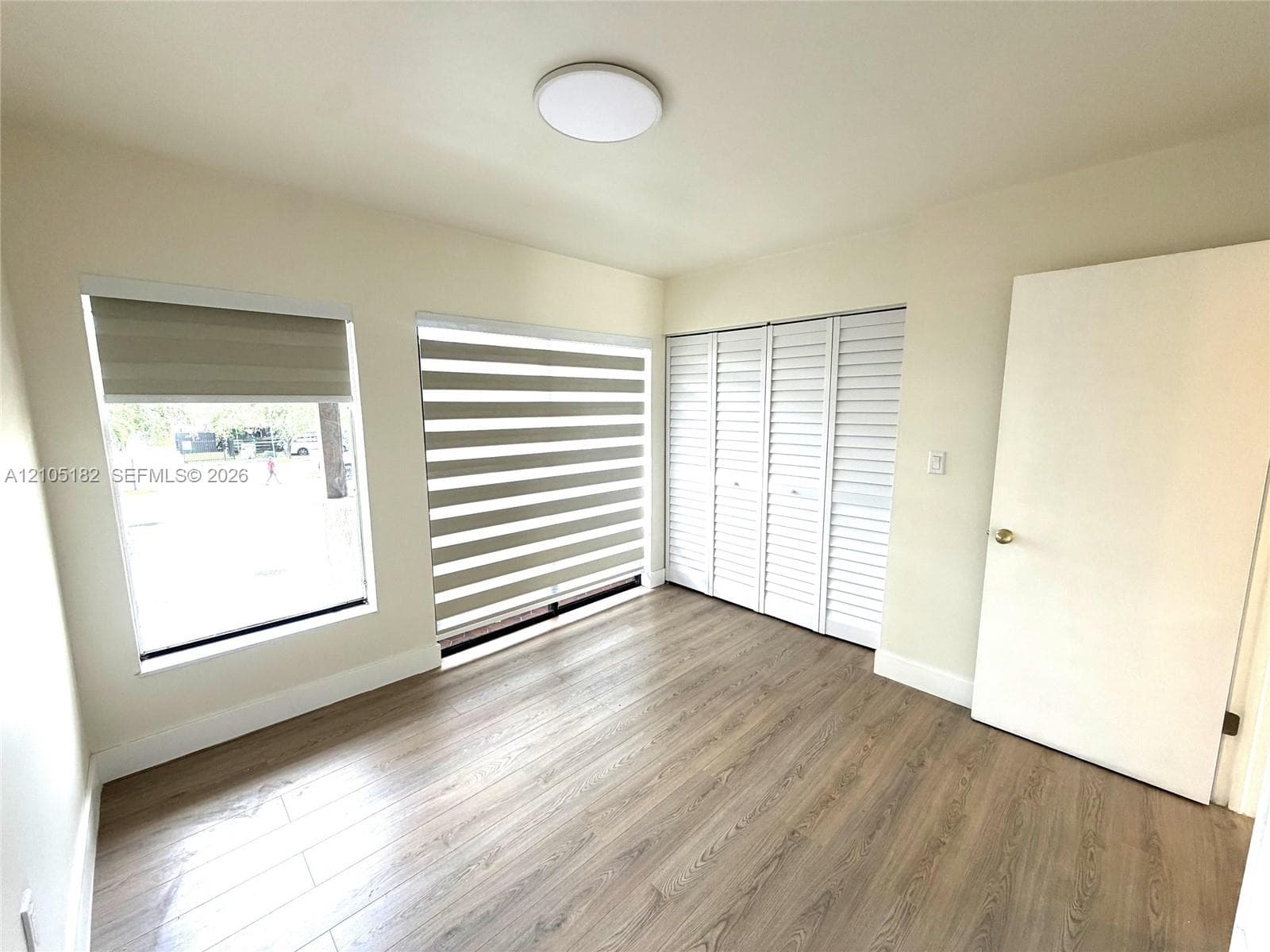 Wood-finish flooring, two windows with blinds, bi-fold closet doors, and a ceiling-mounted light fixture