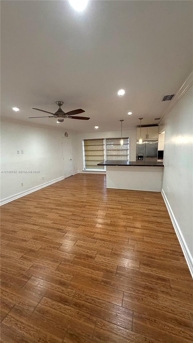 Wood-finish tile flooring throughout, featuring recessed lighting, a ceiling fan, and a kitchen island with pendant lighting