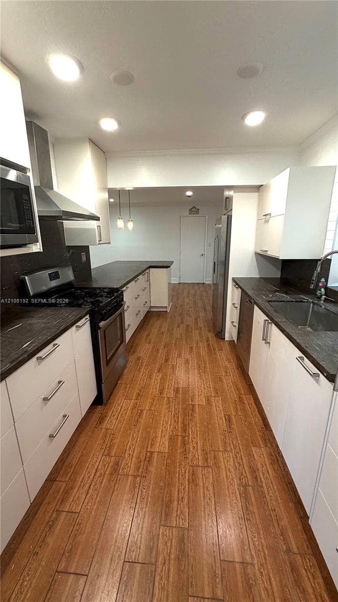 Galley kitchen featuring wood-finish flooring, white cabinetry with stainless steel hardware, dark countertops, and recessed lighting
