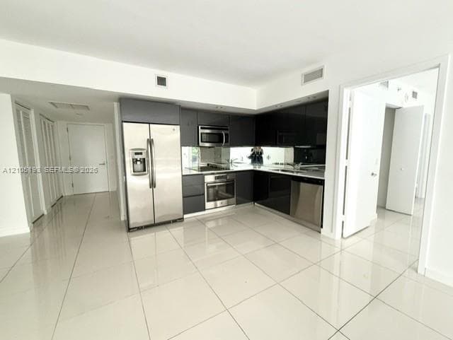 Modern kitchen featuring high-gloss dark cabinetry, stainless steel appliances, a mirrored backsplash, and large-format porcelain tile flooring