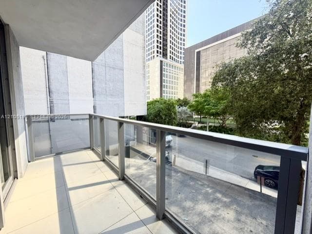 Covered balcony featuring oversized tile flooring, tempered glass railings, and a dark metal frame
