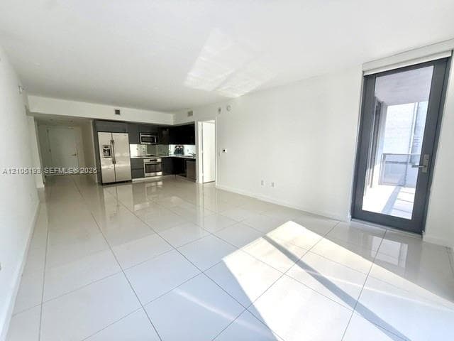 Open floor plan featuring polished tile flooring, kitchen with dark cabinetry, stainless steel appliances, and a glass-paneled exterior door