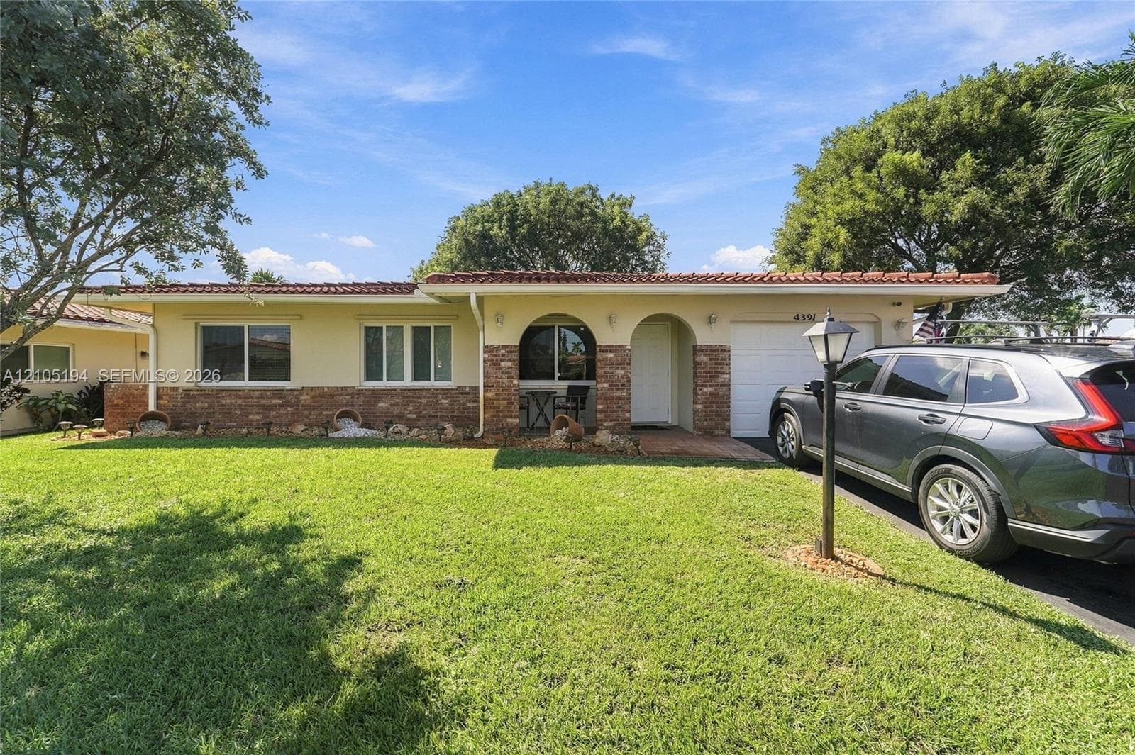 Single-story exterior featuring a textured stucco facade, decorative stone accents, arched entryway, and tile roof