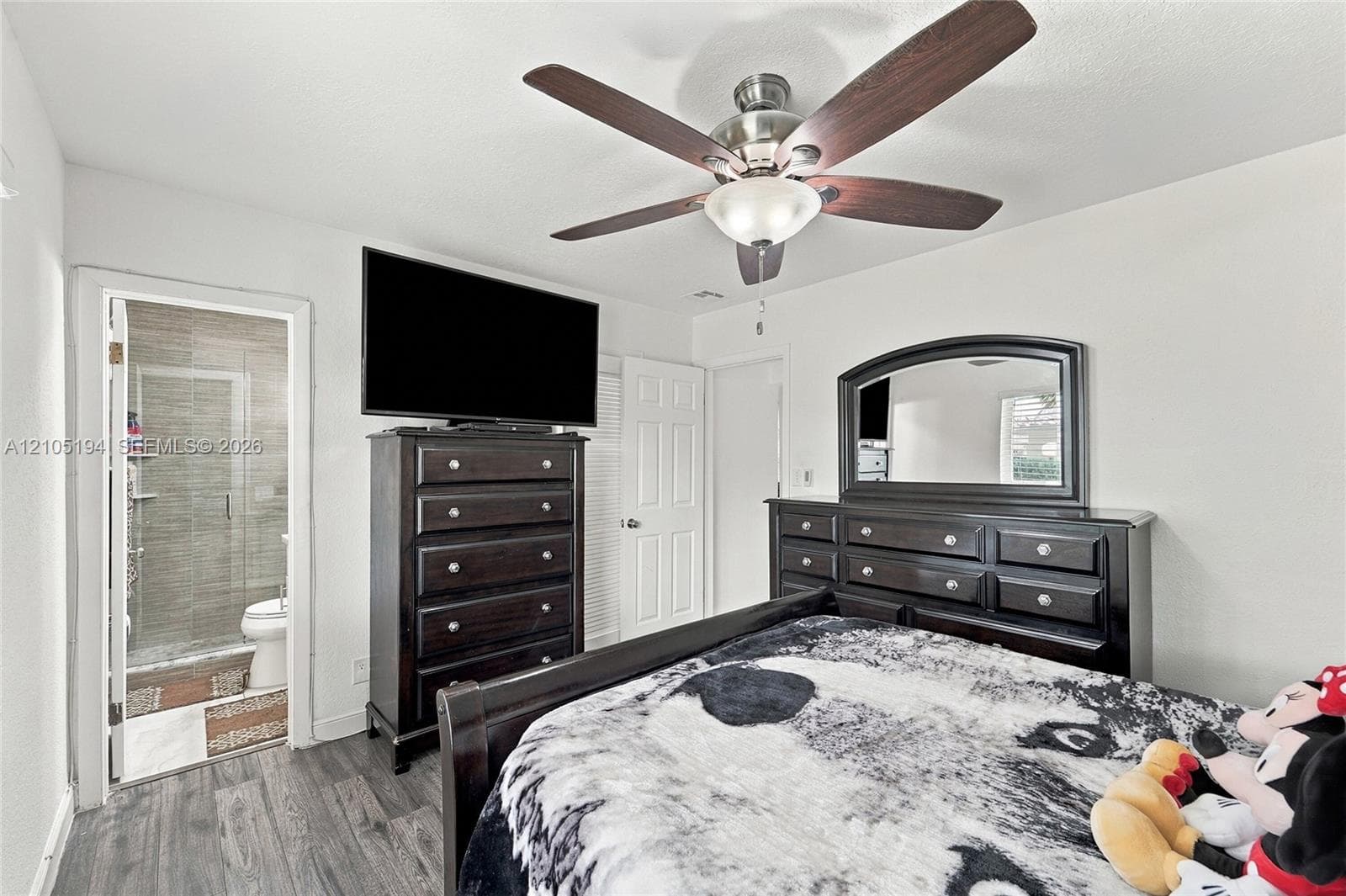Room featuring wood-finish flooring, a multi-blade ceiling fan with integrated lighting, and a doorway entry to a tiled shower area