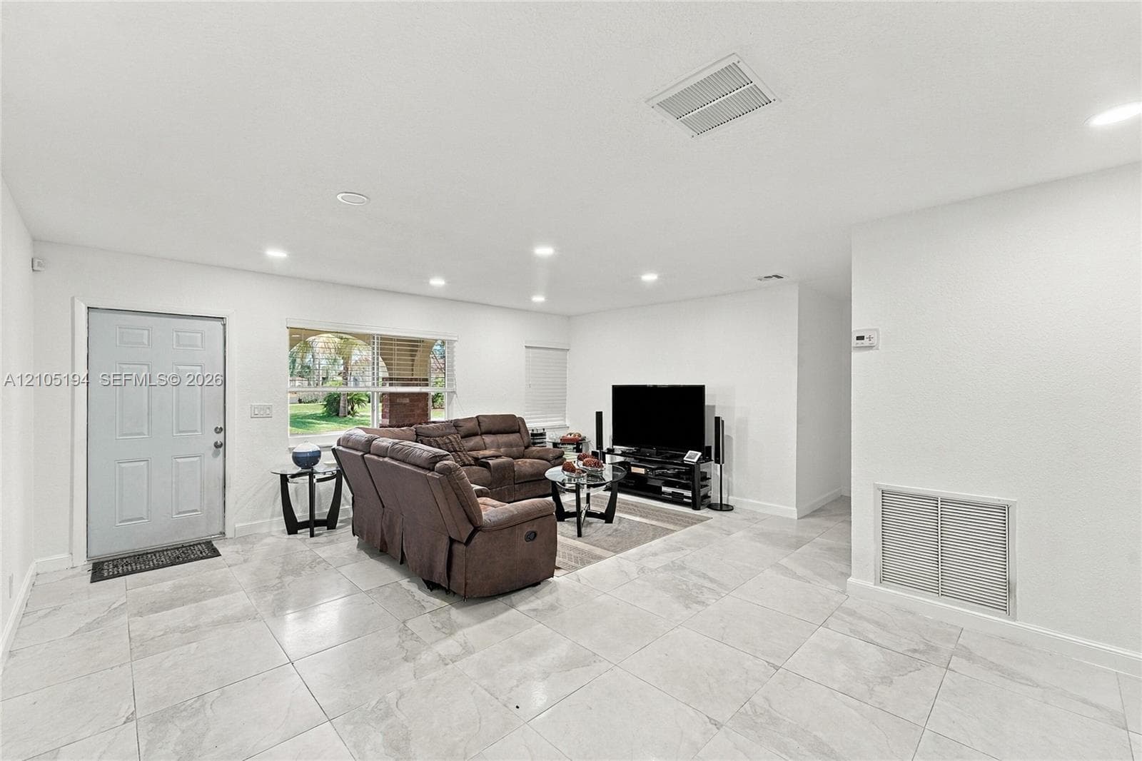 Living area featuring large-format ceramic tile flooring, recessed ceiling lighting, and a multi-panel exterior door