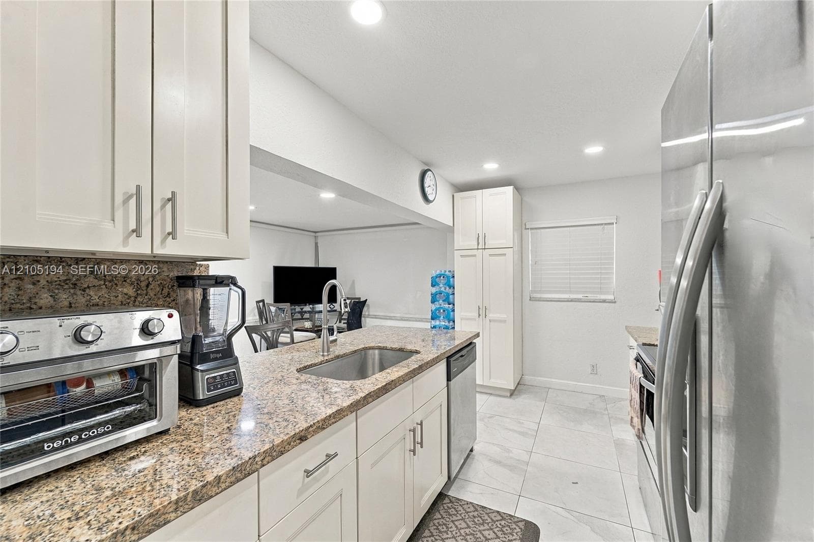 Kitchen featuring stone countertops, white cabinetry with silver-tone hardware, stainless steel undermount sink, recessed lighting, and tile flooring