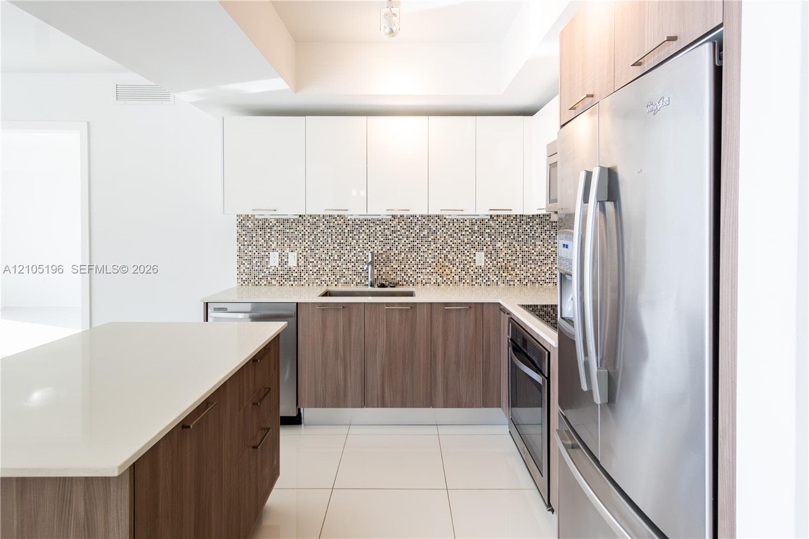 Modern kitchen featuring white cabinetry, wood-finish lower cabinetry, white countertops, mosaic tile backsplash, and stainless steel appliances