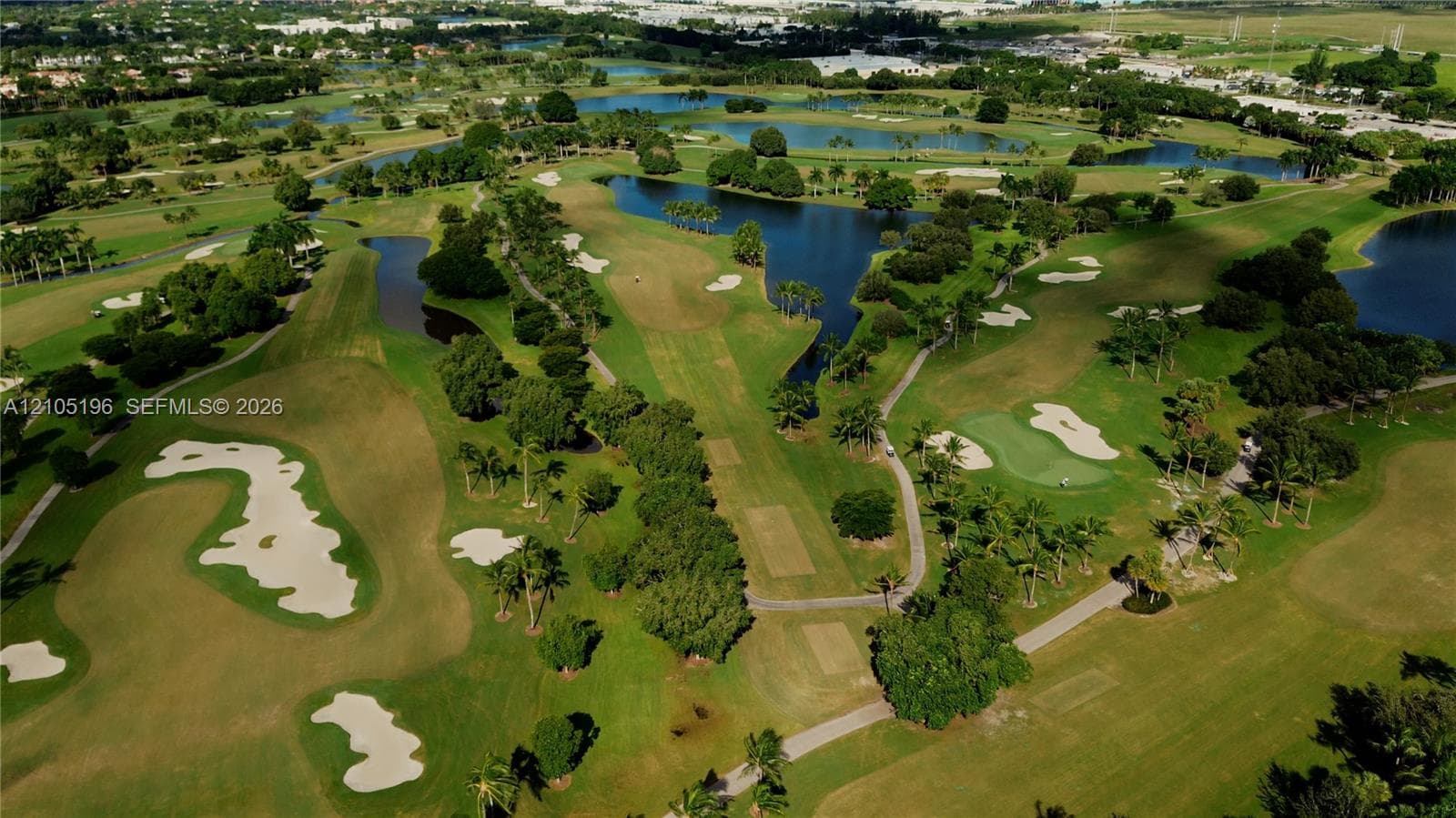 Expansive golf course featuring manicured greens, sand bunkers, and multiple water features surrounded by mature trees