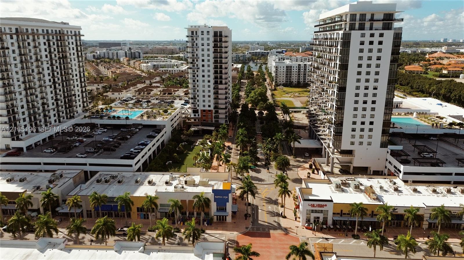 Two high-rise buildings with multiple balconies, a ground-level retail space, and a multi-level parking structure featuring a rooftop pool