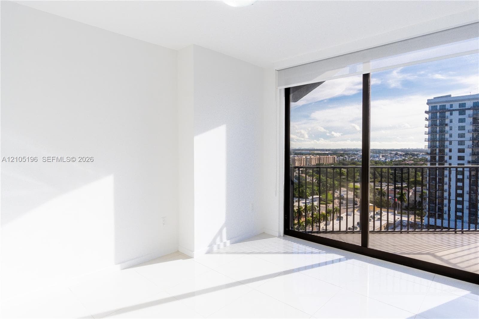 Expansive full-height glass sliding doors, white tile flooring, and a balcony with metal railings