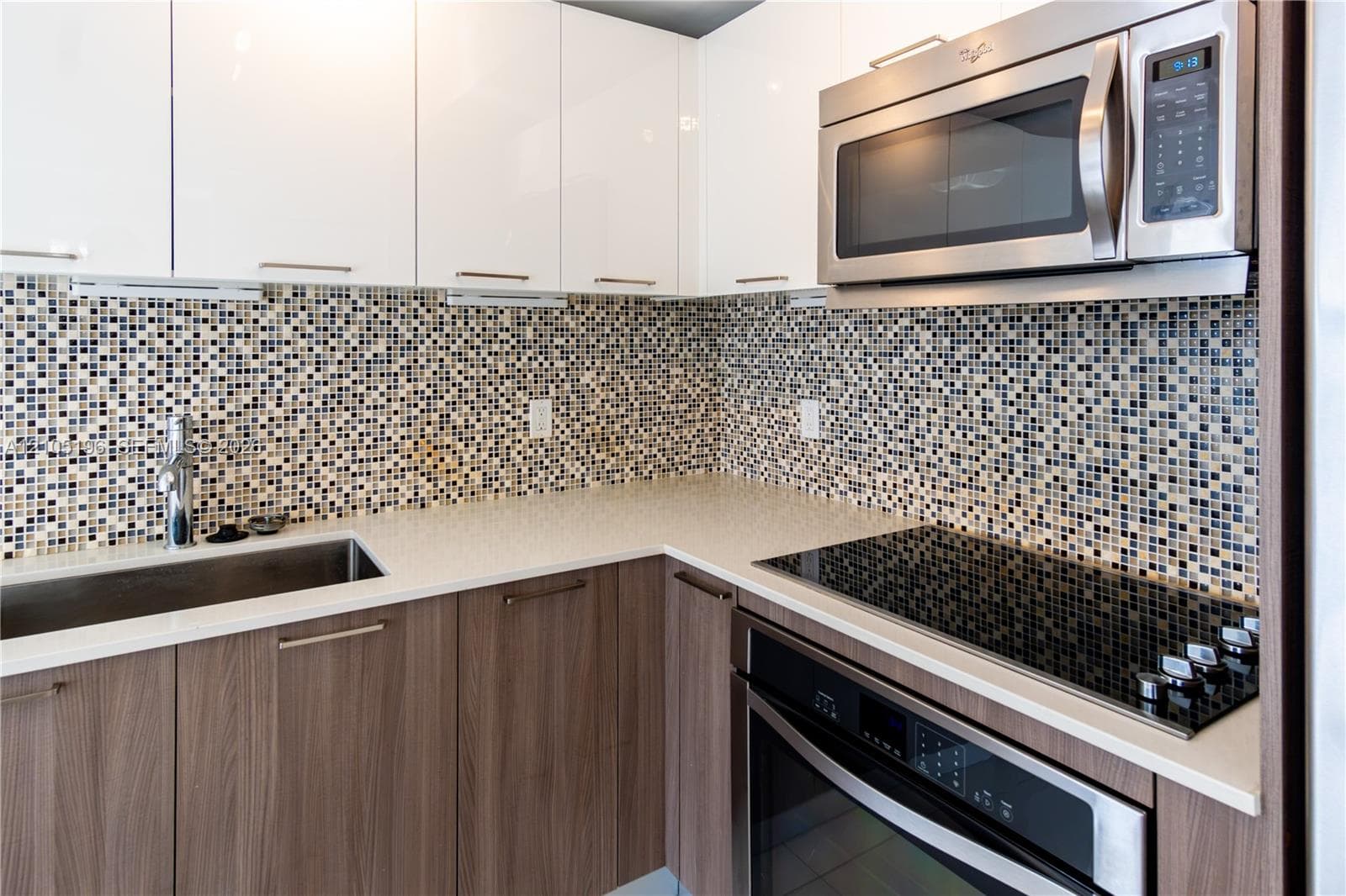 Kitchen featuring a mosaic tile backsplash, stainless steel appliances, wood-finish lower cabinetry, white upper cabinetry, and a solid surface countertop