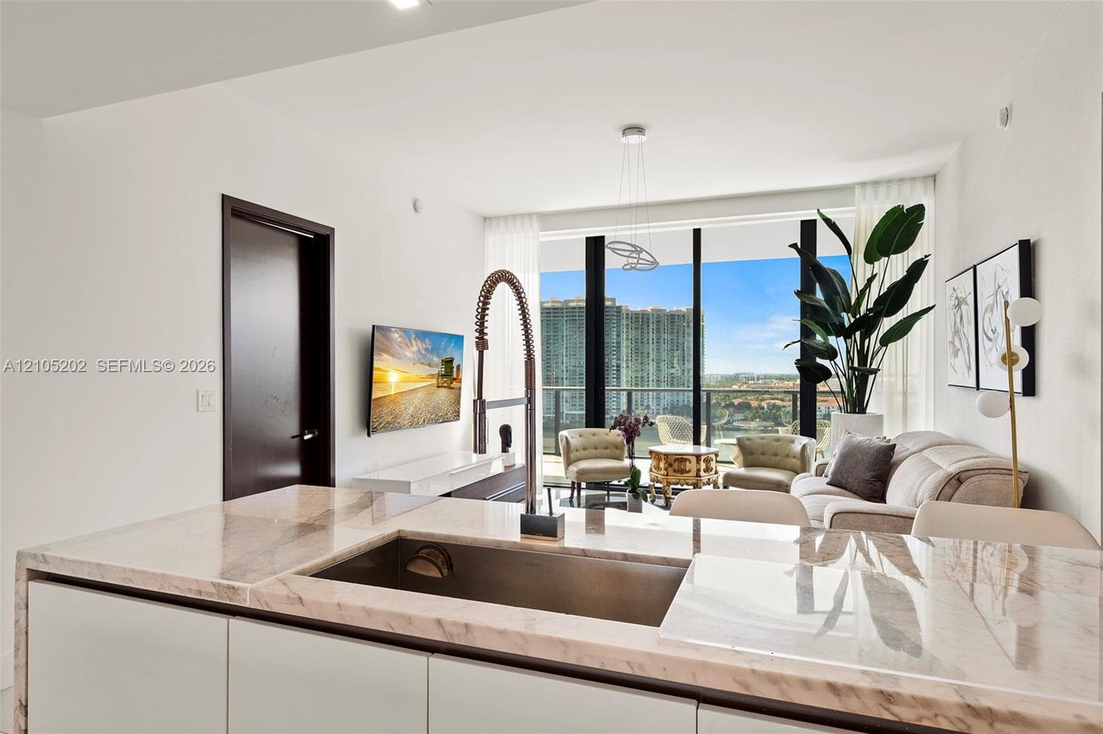 Kitchen island featuring stone countertop, undermount stainless steel sink, and high-arc faucet, complemented by floor-to-ceiling windows and balcony access