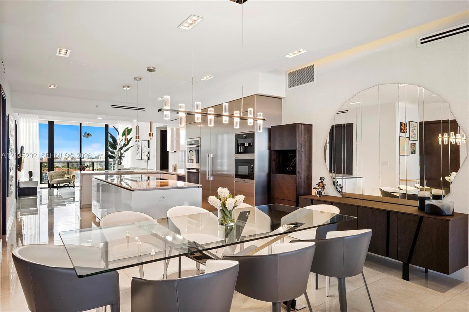 Kitchen featuring a large central island with a stone countertop, built-in stainless steel appliances, multi-light glass pendant fixtures, and polished tile flooring