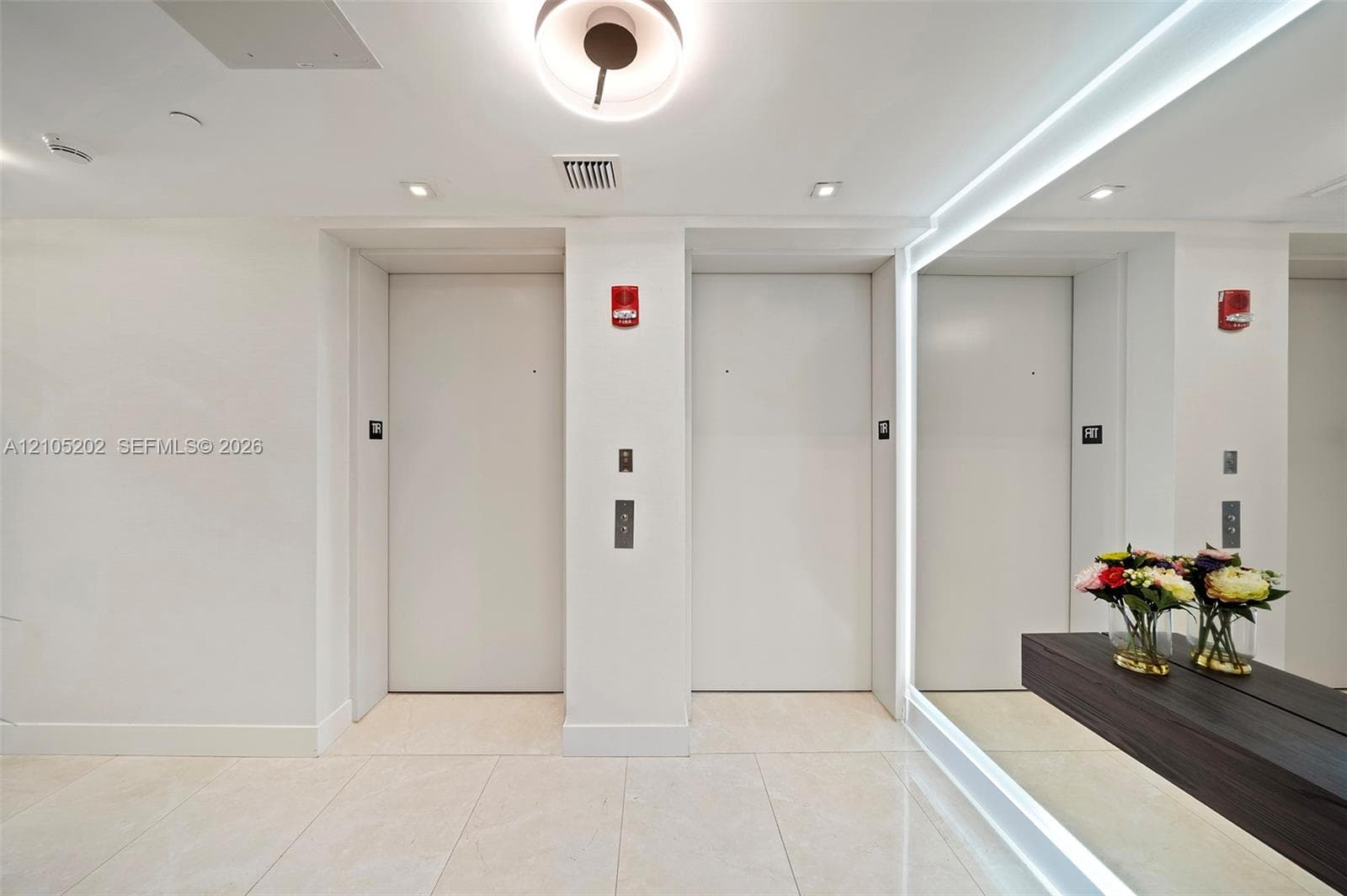 Dual elevator lobby featuring large-format tile flooring, recessed ceiling lighting, and a full-length wall mirror