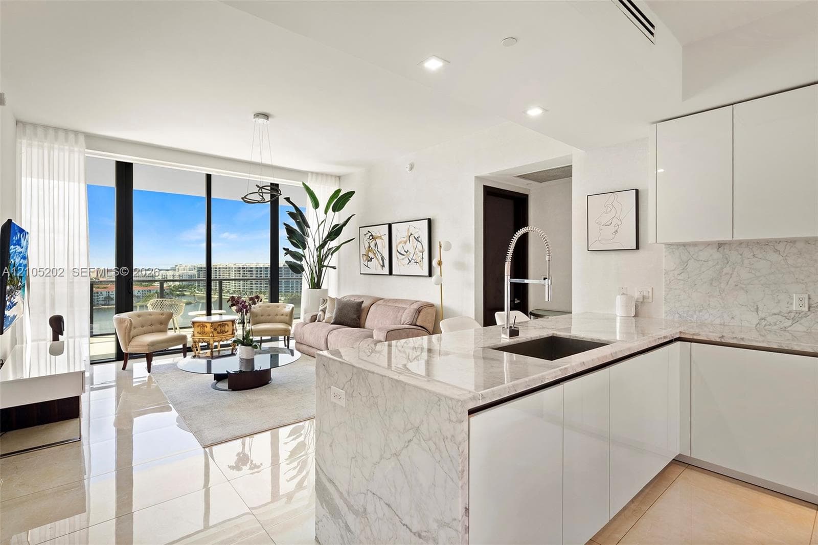 Kitchen featuring high-gloss cabinetry, stone-surface waterfall island, and undermount stainless steel sink with gooseneck faucet, highlighted by floor-to-ceiling windows and polished stone flooring