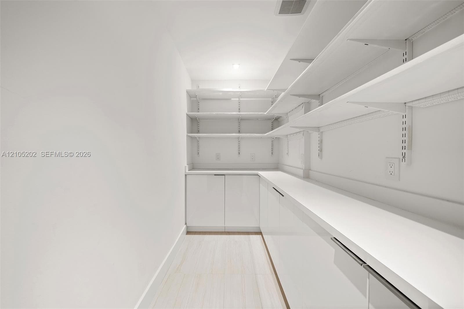Storage area featuring floor-to-ceiling adjustable shelving, extensive solid-surface countertops, high-gloss cabinetry, and light-toned flooring