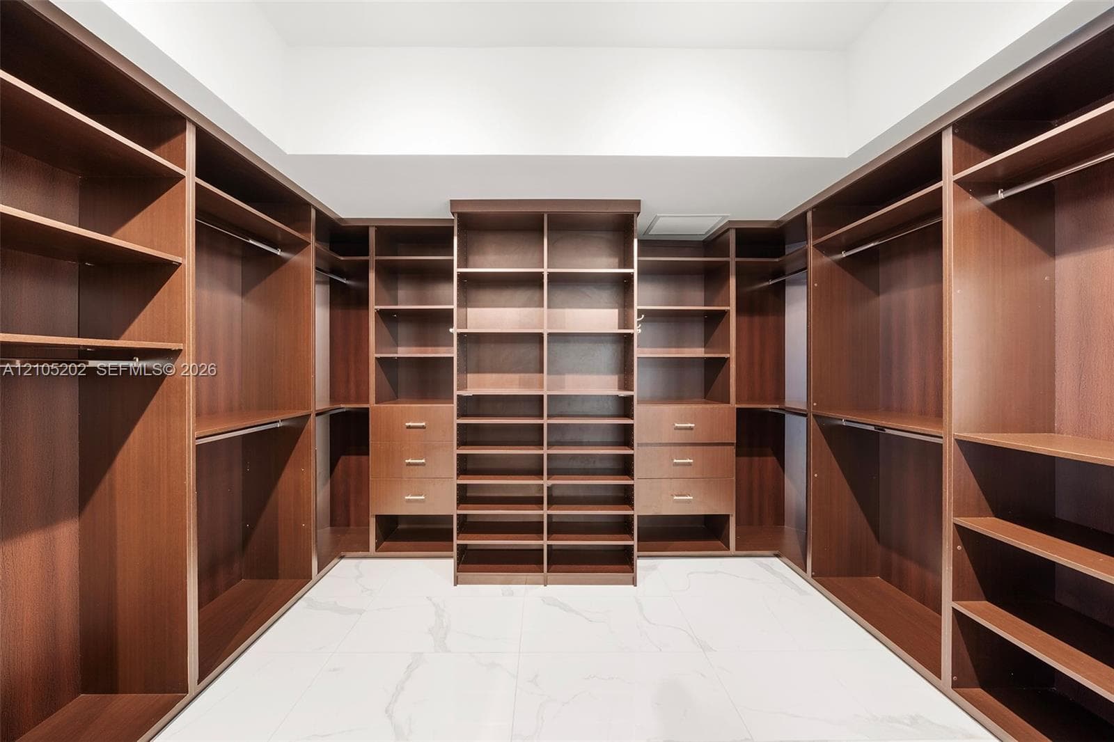 Custom wood-finish cabinetry featuring open shelving, integrated hanging rods, and six built-in storage drawers, complemented by white stone-finish flooring