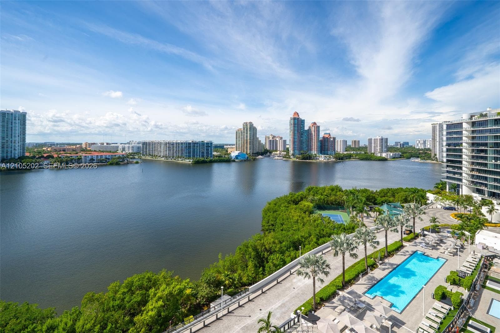 Waterfront setting featuring a swimming pool, tennis court, paved walking path, and mature tropical landscaping