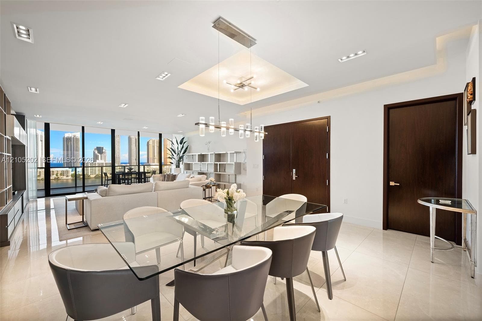 Open-concept space featuring polished stone flooring, recessed lighting, a recessed ceiling tray, a linear multi-light pendant fixture, and floor-to-ceiling windows
