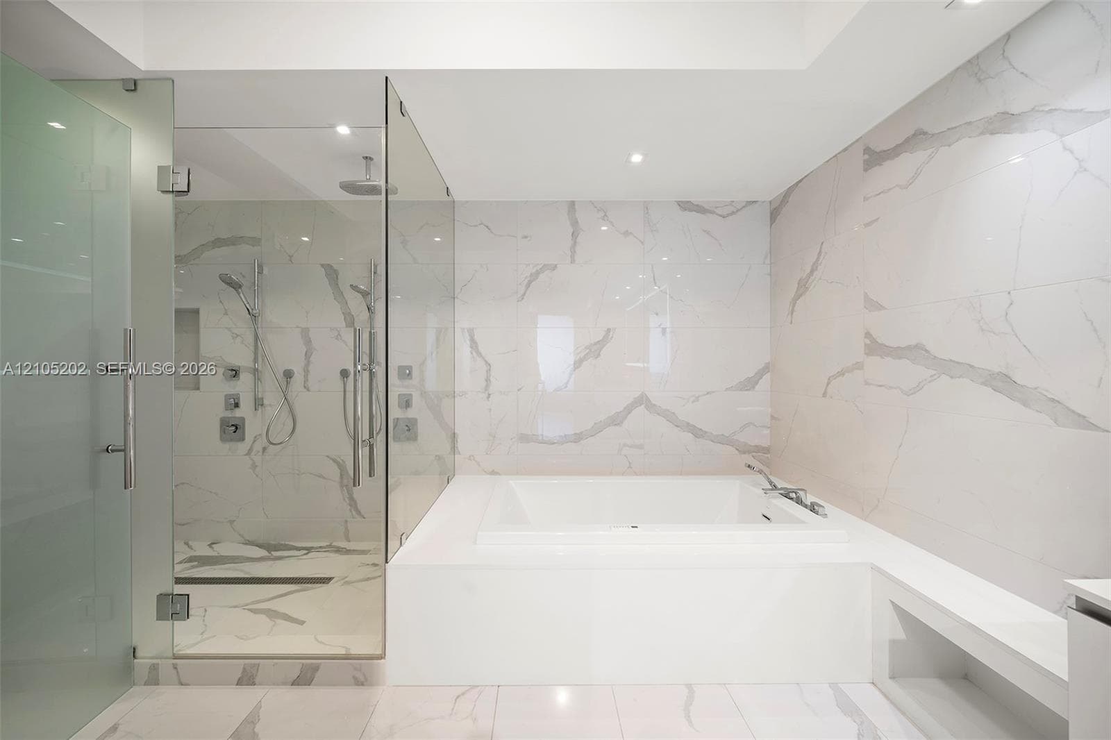 Enclosed glass shower featuring dual shower heads and a built-in recessed niche, complemented by a deep soaking tub surrounded by full-height stone-finish wall tiling and matching floor tile