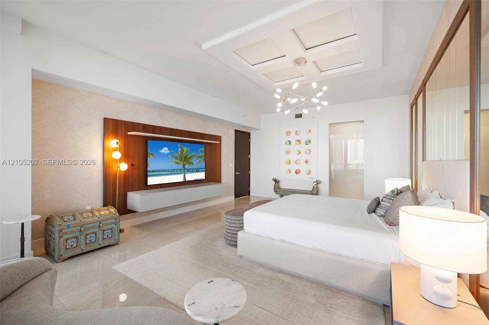 Coffered ceiling with modern multi-arm chandelier, wall-mounted wood-panel media feature, floating cabinetry, and tile flooring