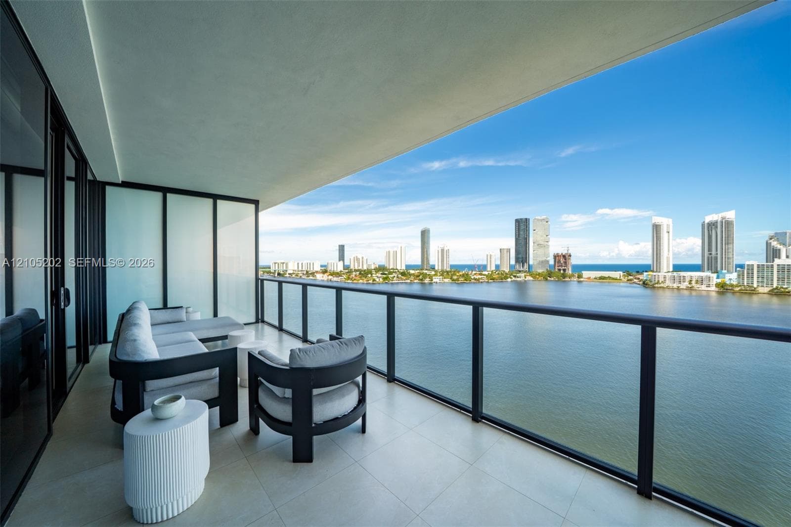 Covered balcony with large-format tile flooring, black metal railing, and expansive water and urban skyline backdrop