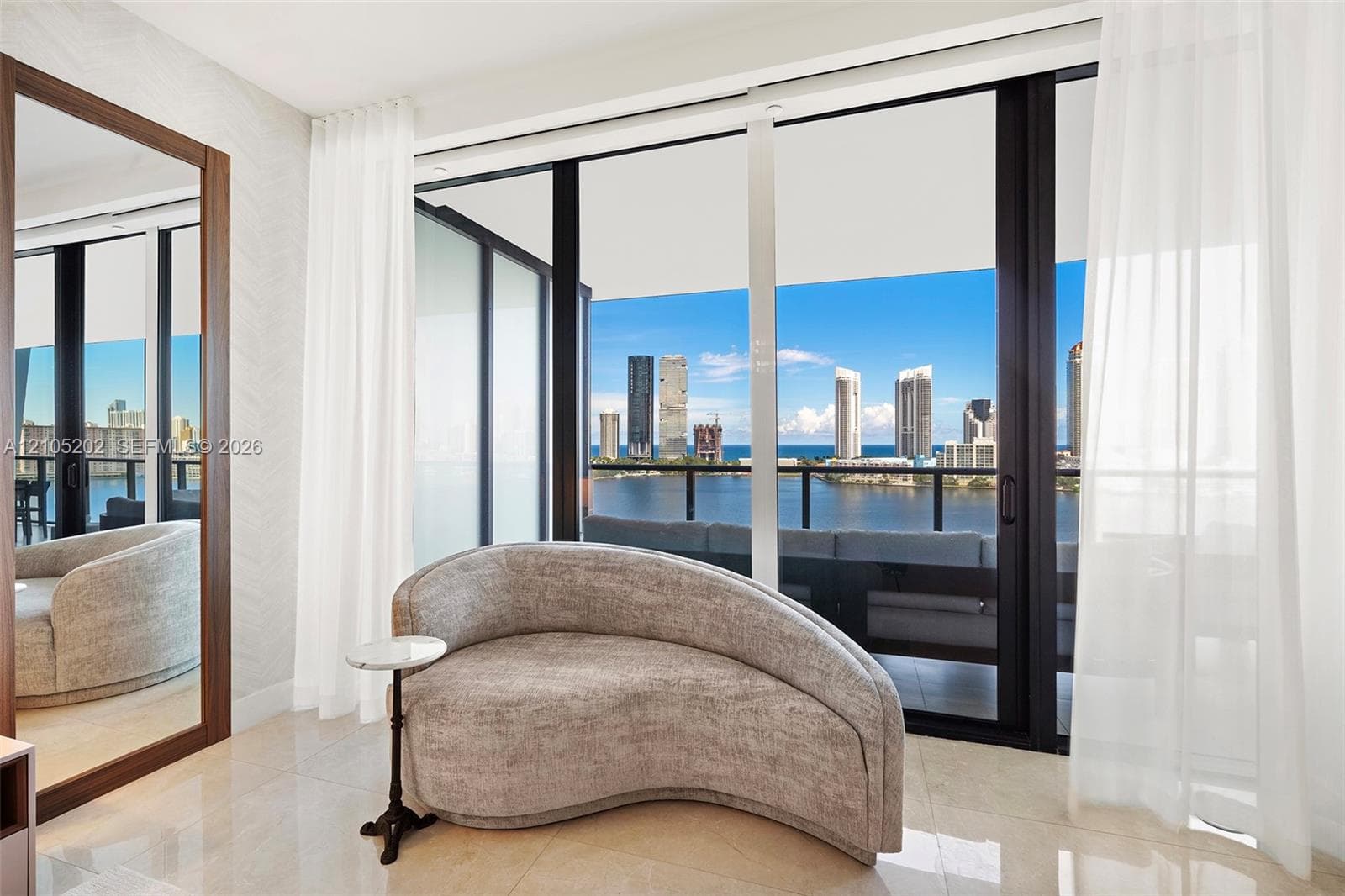 Floor-to-ceiling sliding glass doors, balcony with black metal railings, polished stone flooring, and expansive urban skyline backdrop
