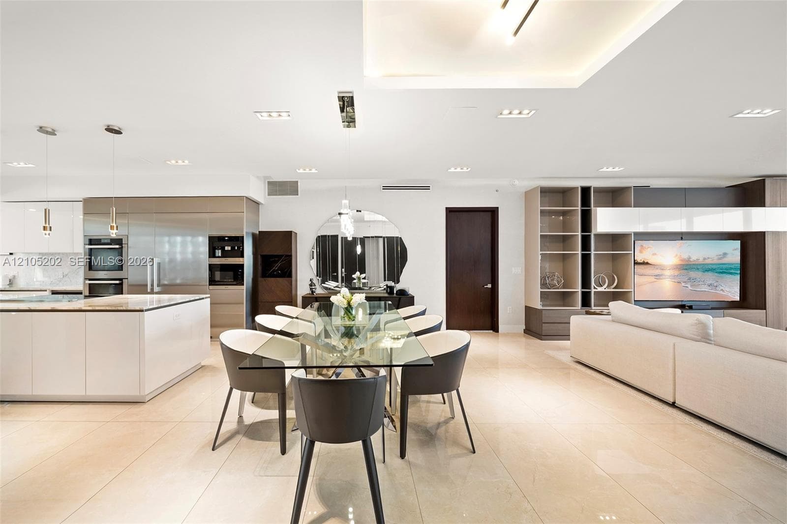 Open-concept living space featuring high-gloss cabinetry, large-format tile flooring, recessed cove lighting, and a custom built-in media shelving unit