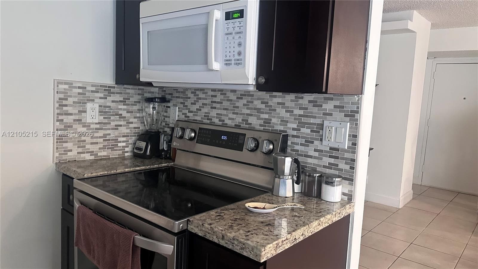Kitchen featuring dark cabinetry, stone-finish countertops, stainless steel range, white over-the-range microwave, and a multicolored glass tile backsplash