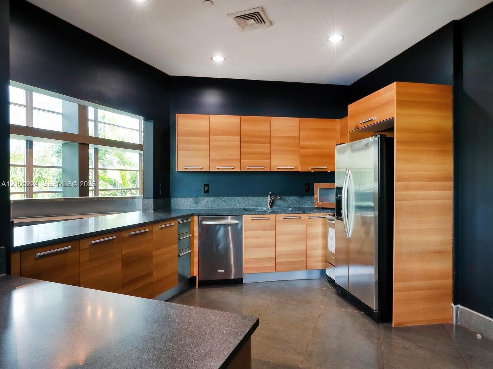 Full-size stainless steel refrigerator, wood-finish cabinetry, built-in stainless steel dishwasher, stone countertops, and recessed lighting