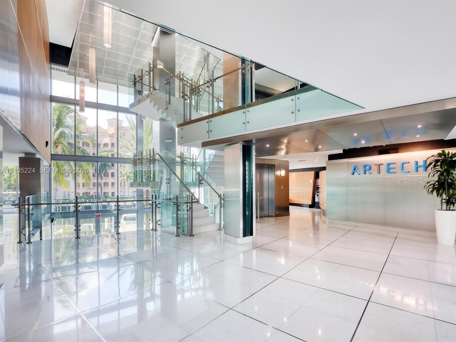 Expansive lobby featuring polished tile flooring, a multi-level staircase with glass railings, full-height windows, and recessed lighting