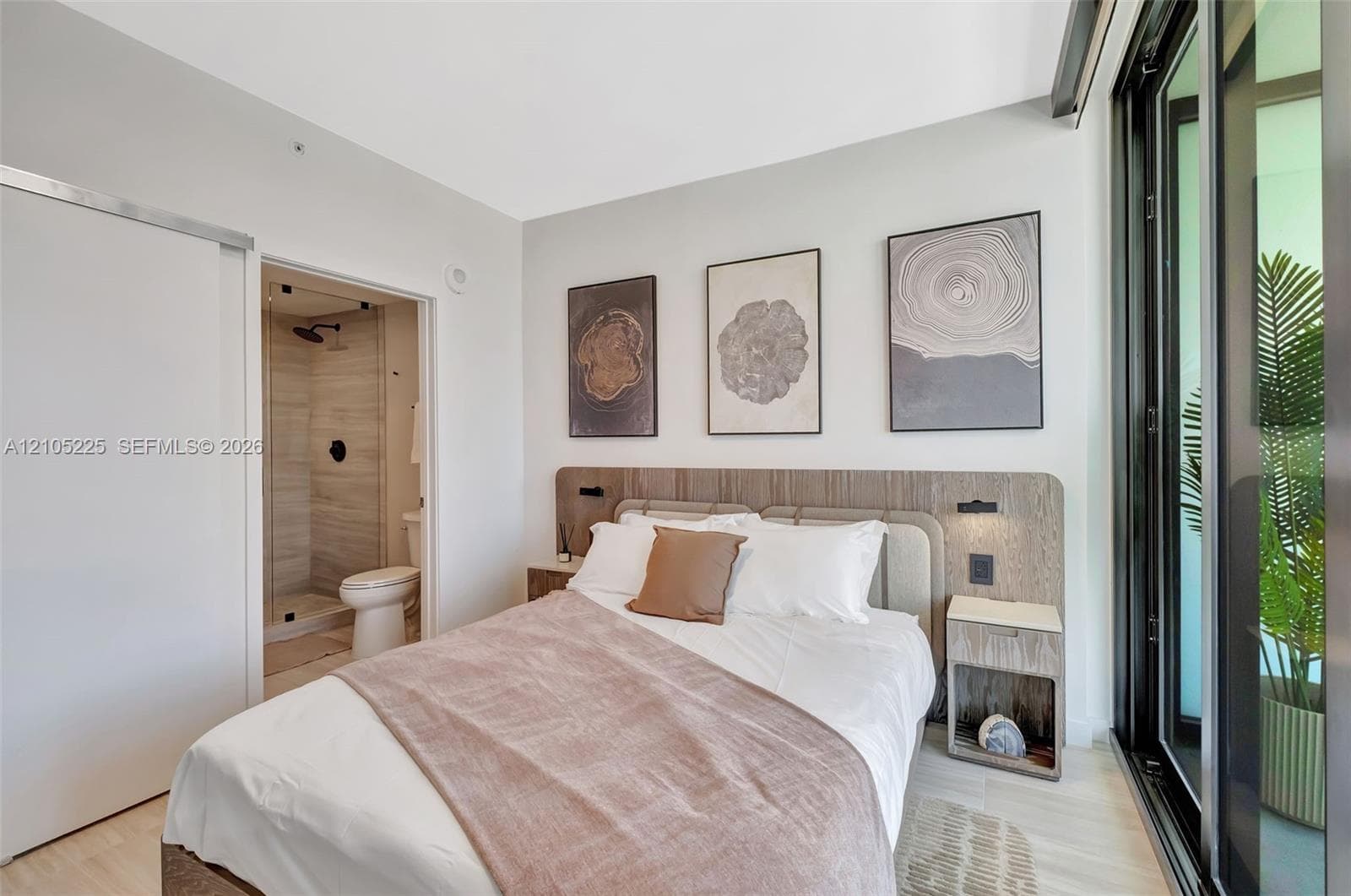 Light wood-finish flooring, built-in headboard with integrated lighting, attached nightstands, and a full-height sliding glass door
