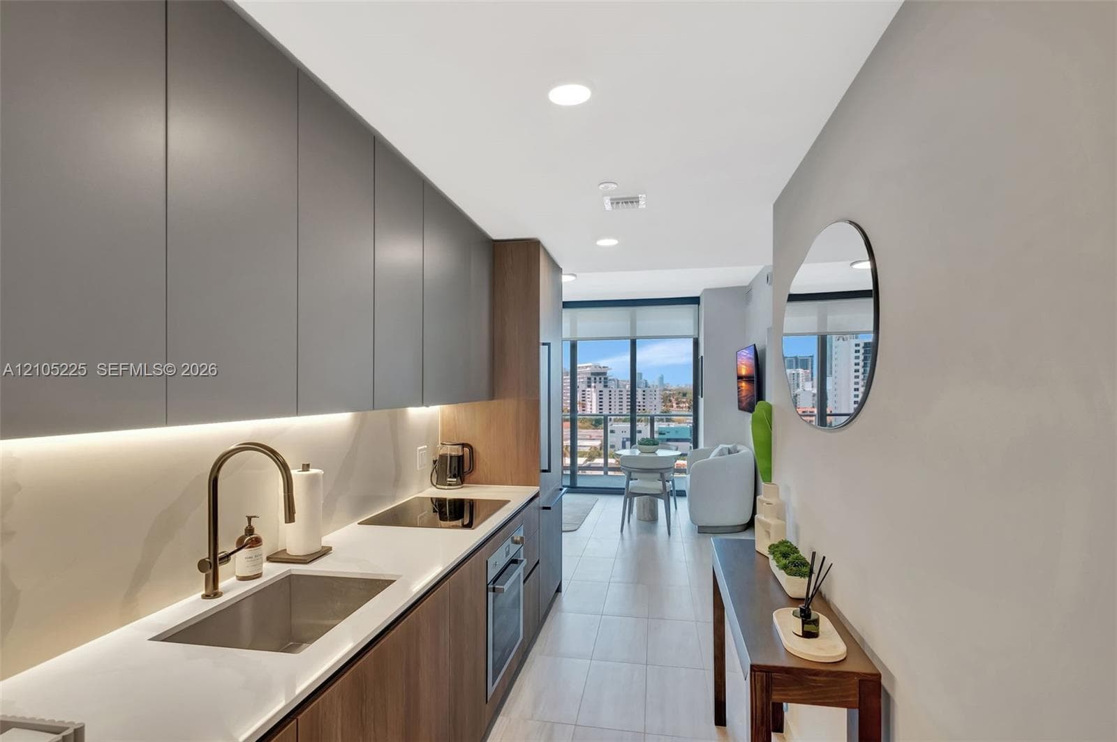 Galley kitchen featuring flat-panel cabinetry, integrated under-cabinet lighting, a built-in cooktop, and a stainless steel sink with a bronze-tone faucet