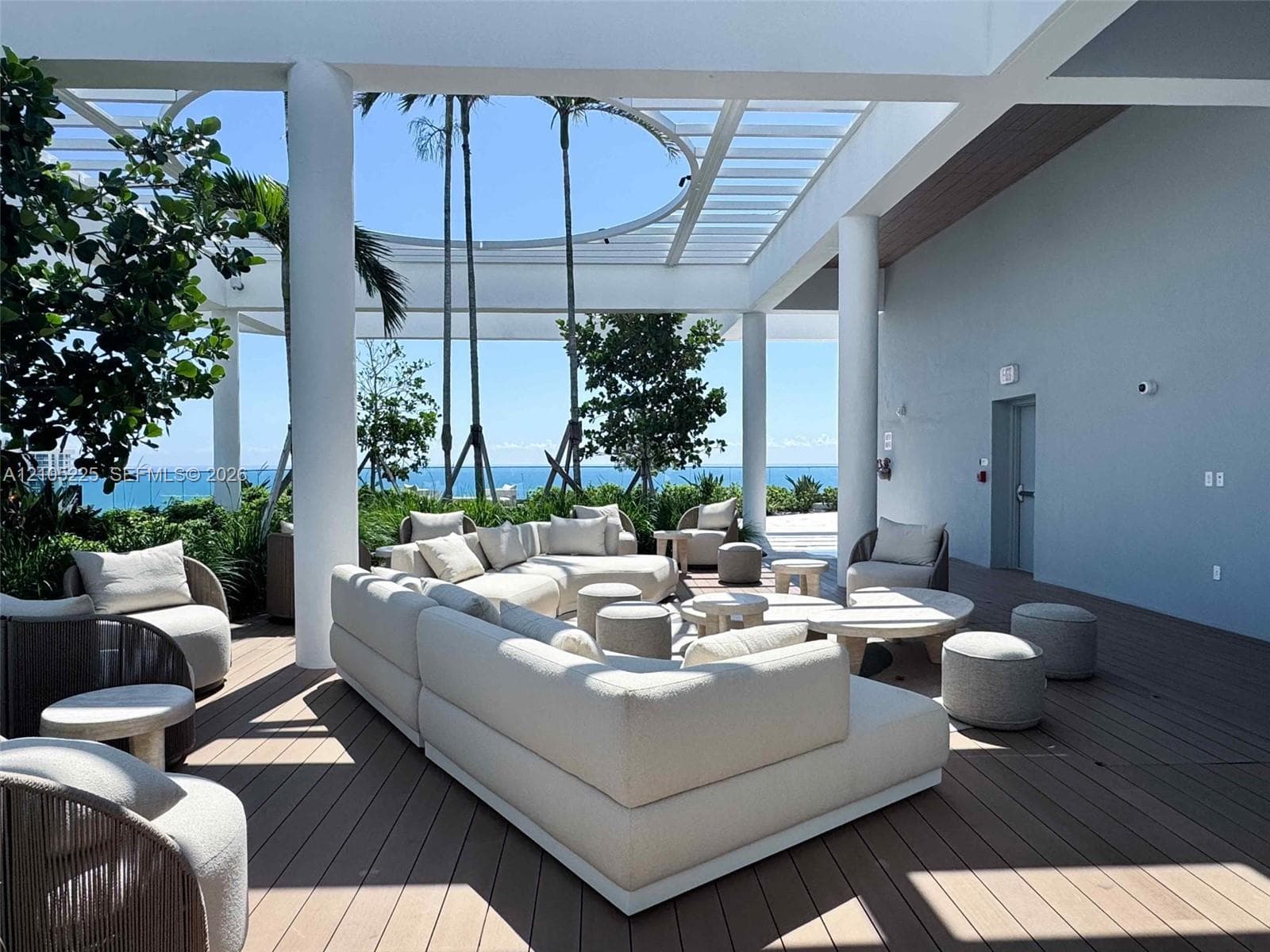 Expansive outdoor terrace featuring slatted wood-finish flooring, a white pergola structure, and mature perimeter landscaping