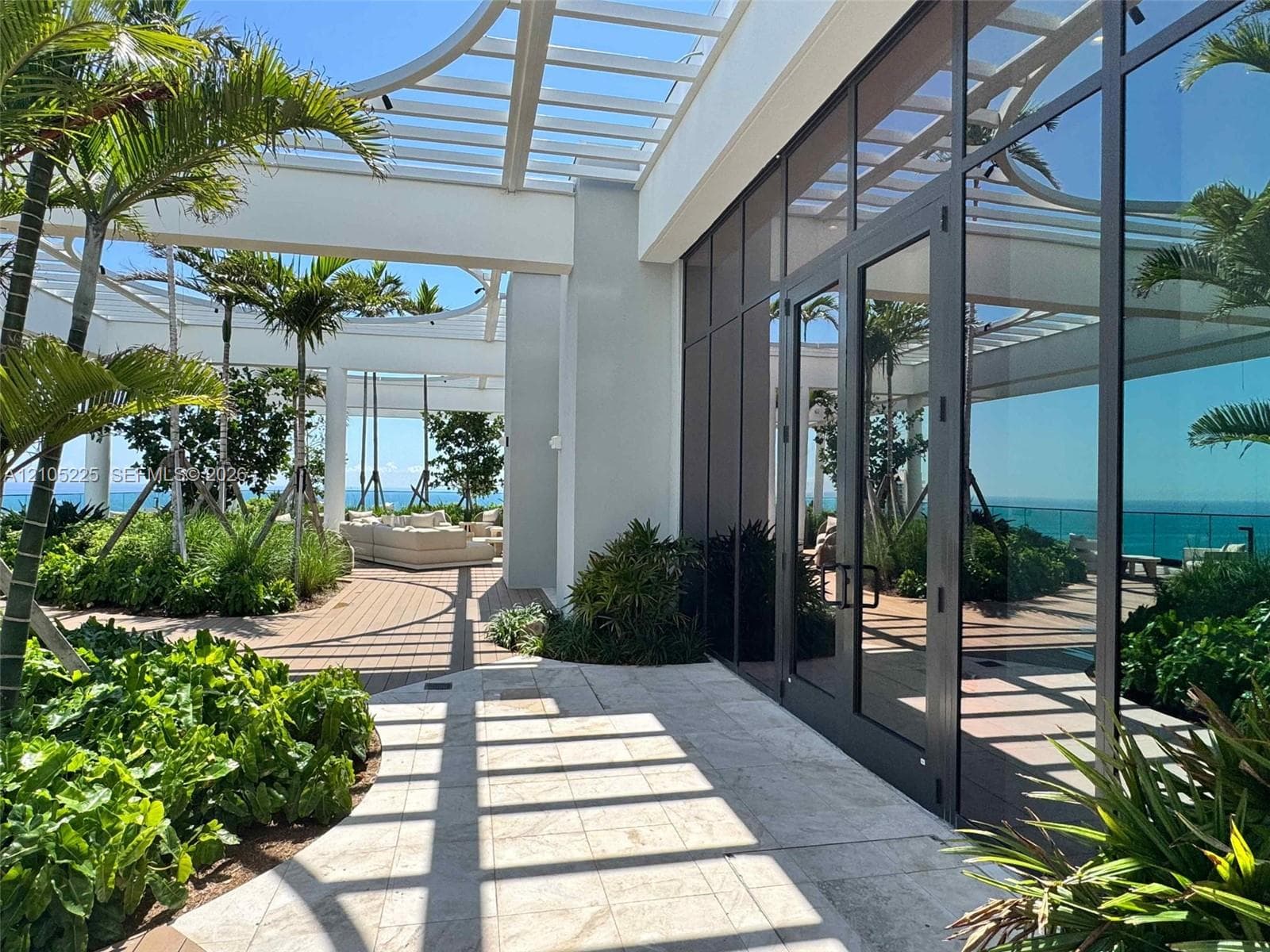 Expansive outdoor terrace featuring mature palm trees, lush landscaping, and a slatted pergola