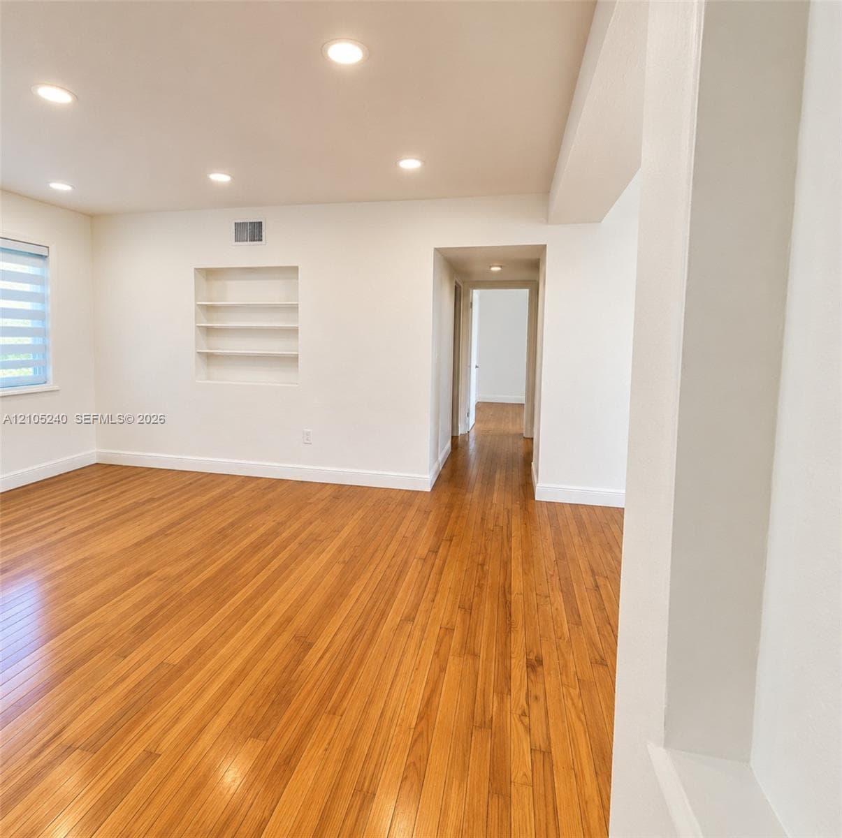 Interior space featuring wood-finish flooring, recessed lighting, built-in wall shelving, and windows with horizontal blinds