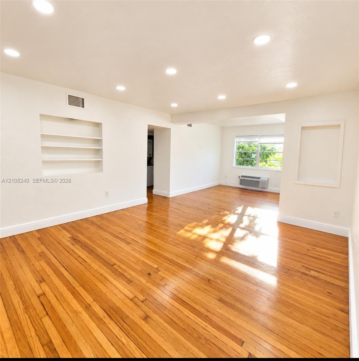 Interior space featuring wood-finish flooring, recessed lighting, built-in wall shelving, and a wall-mounted climate control unit