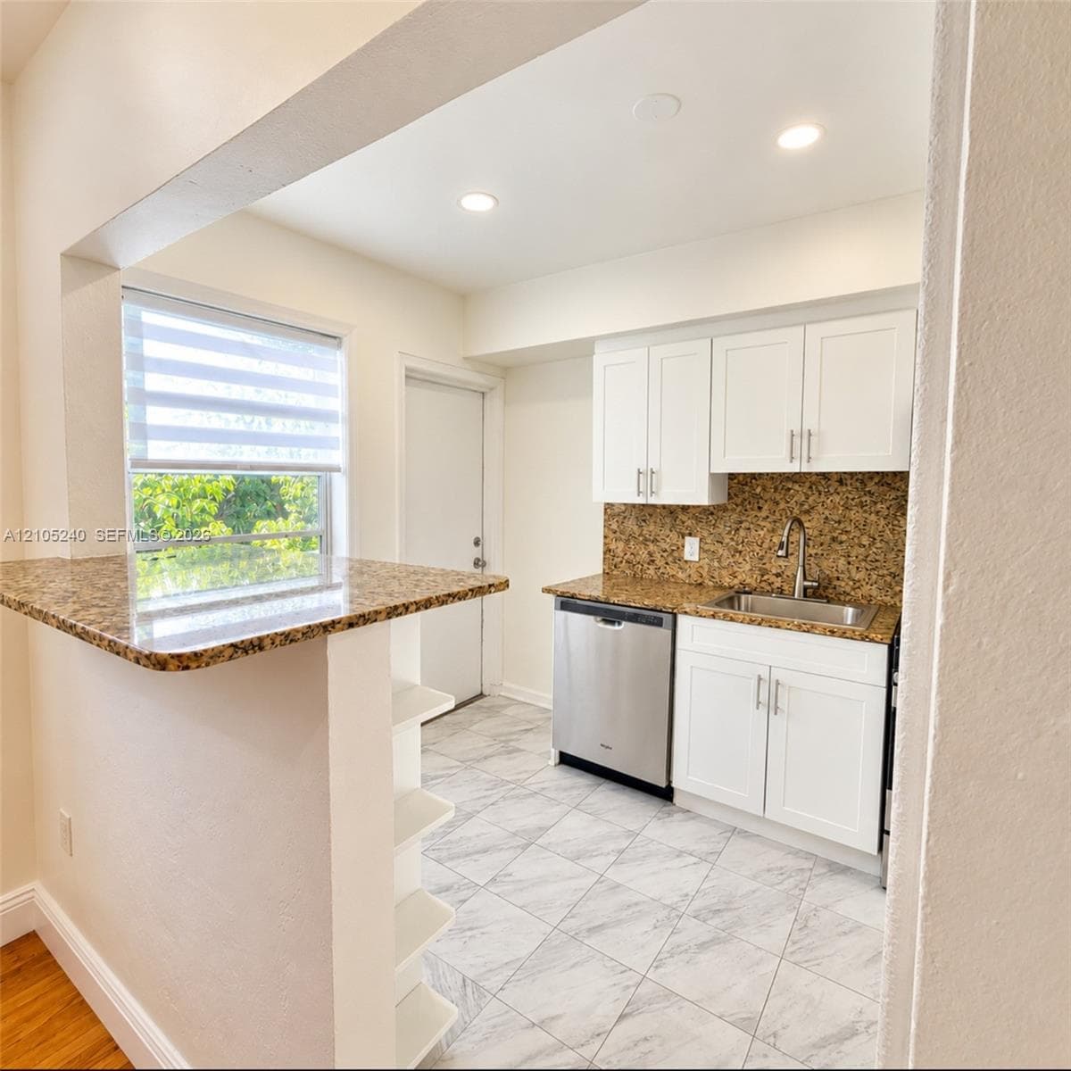 Kitchen area featuring white cabinetry, stone-finish countertops, stainless steel dishwasher, undermount sink with a gooseneck faucet, and tile flooring