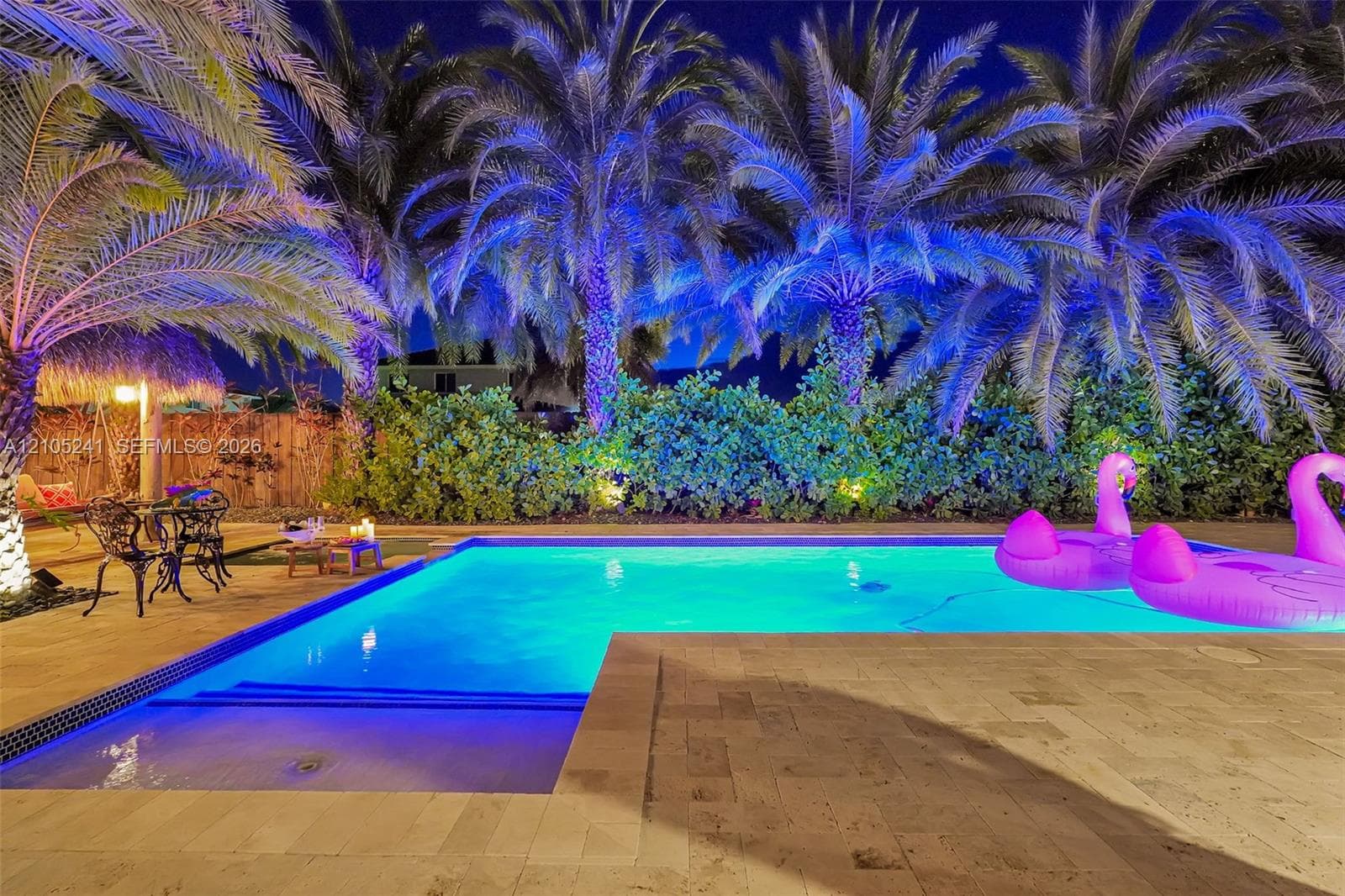 Swimming pool with underwater lighting, surrounded by a paved deck and mature palm trees