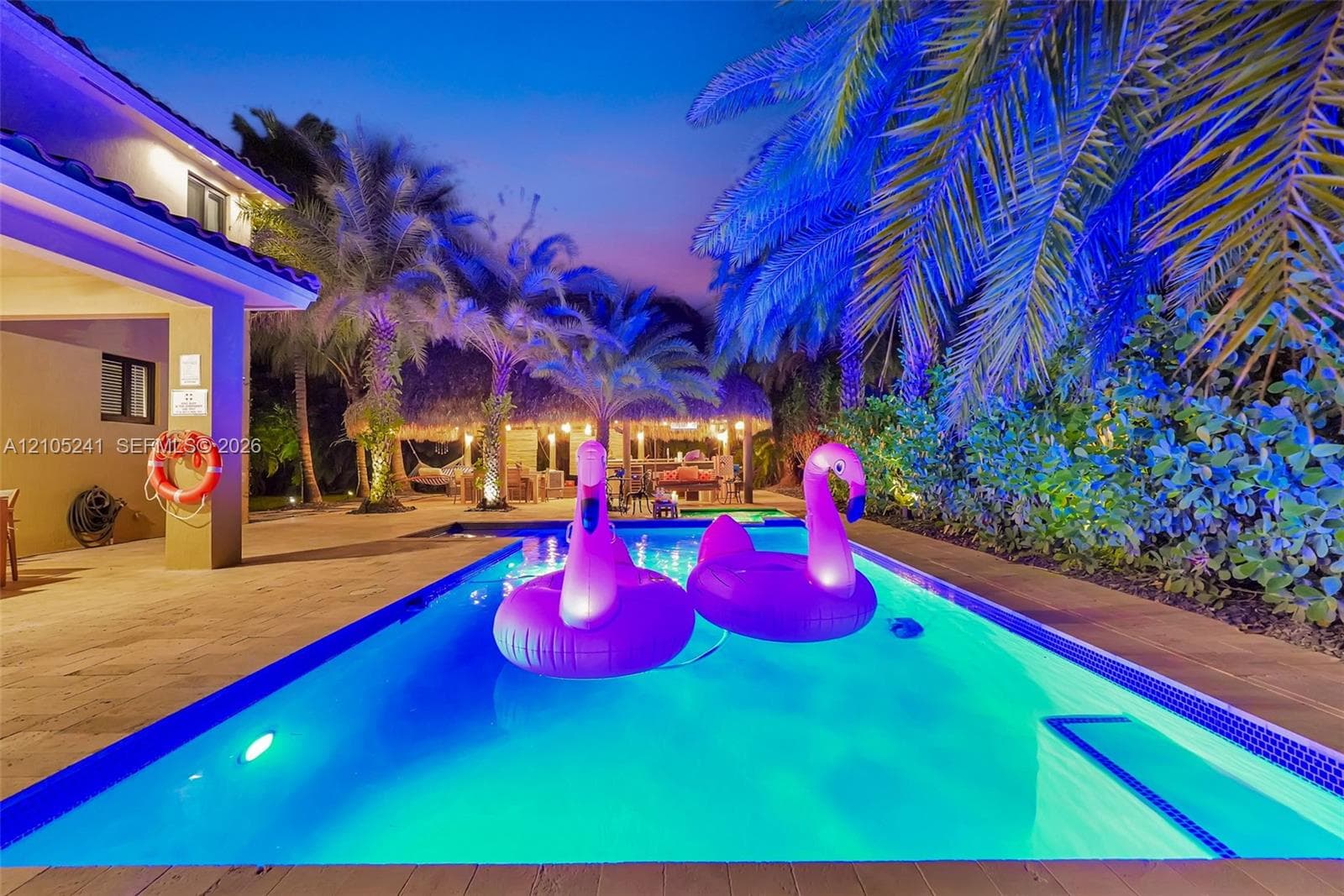 Resort-style pool with integrated lighting, surrounded by a paved patio and mature palm trees