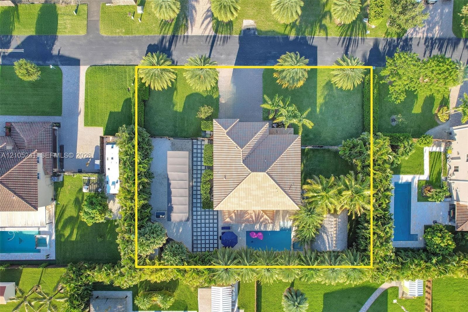 Aerial perspective of a property featuring a hip roof structure, a rectangular swimming pool, integrated paver hardscaping, and mature perimeter landscaping